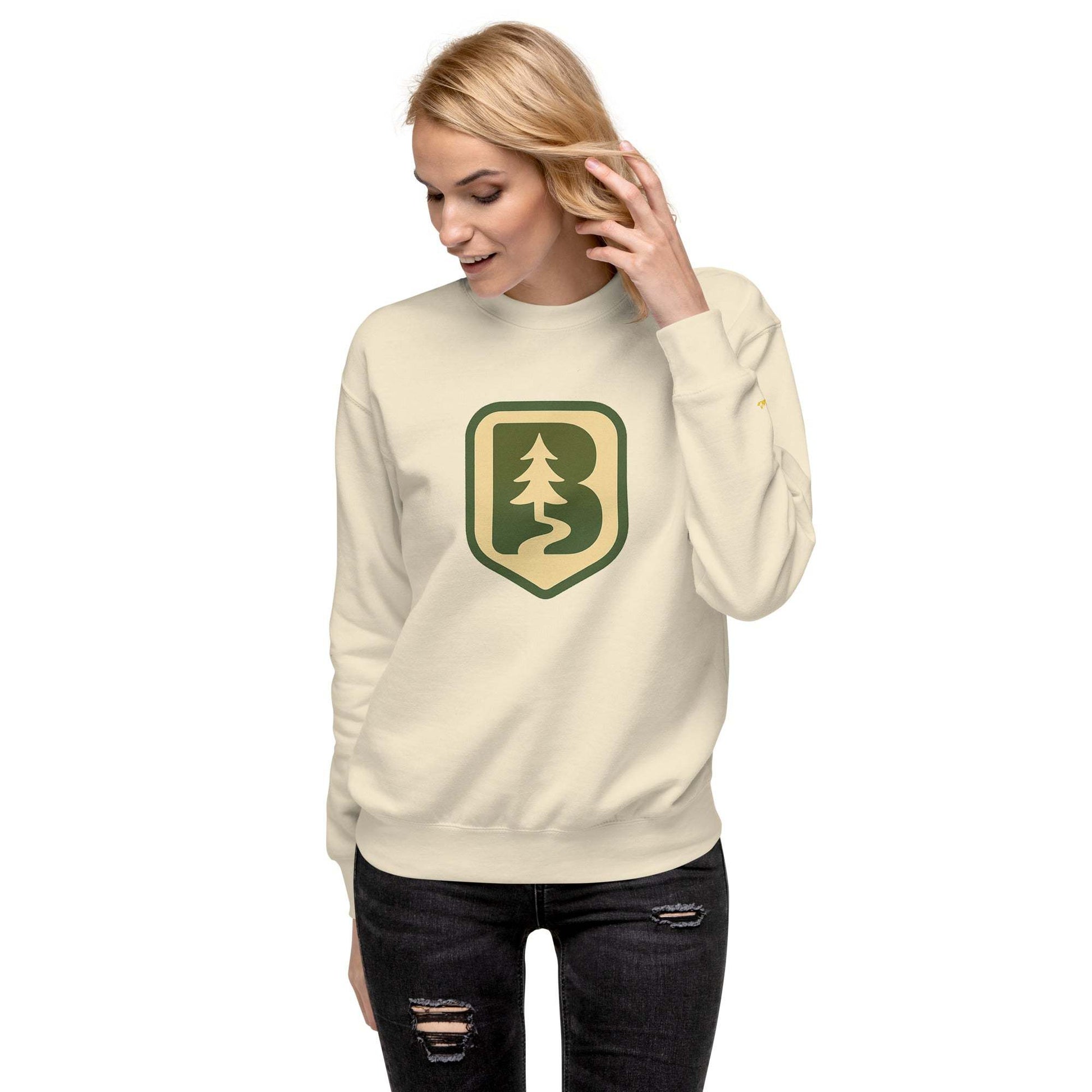 Woman wearing 70s Boise Unisex Sweatshirt in cream with forest logo, ribbed crew neck and cuffs, paired with ripped black jeans